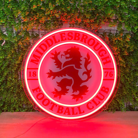 A circular red neon-style sign for Middlesbrough Football Club, featuring the club's lion emblem in the center, displayed against a green ivy-covered wall.
